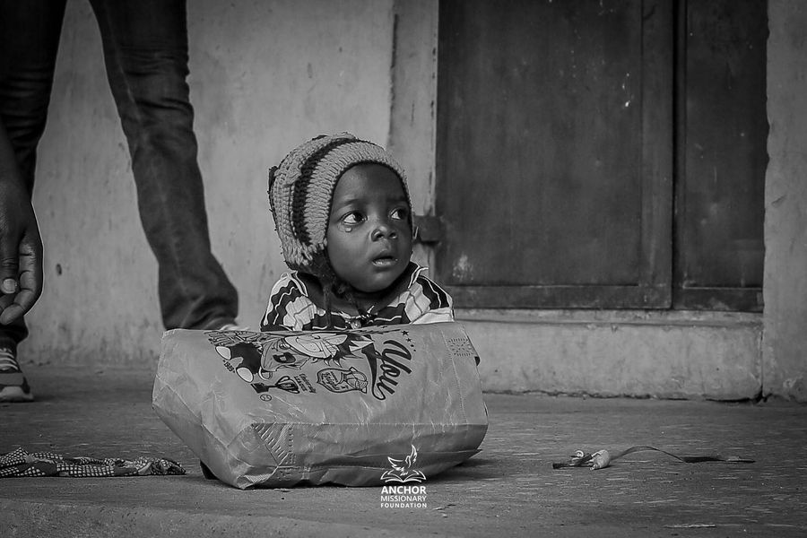 A child waits quietly beside a bag of relief supplies